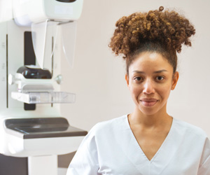 Smiling woman nurse with a mammography machine in background