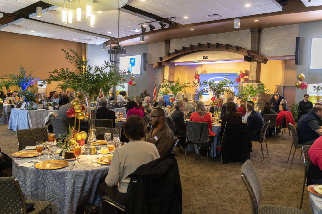 People are shown sitting at big round tables in a decorated room for the awards luncheon.