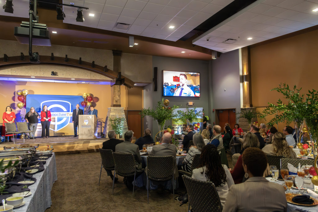 View of the stage with Chris Monroe and finalists, and people seated at tables